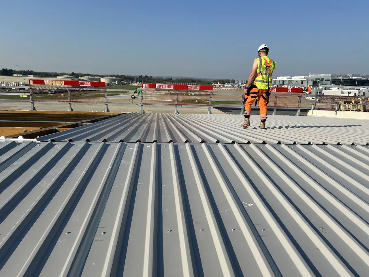 A roofer in a safety harness walking a newly installed standing seam roof at Gatwick Airport