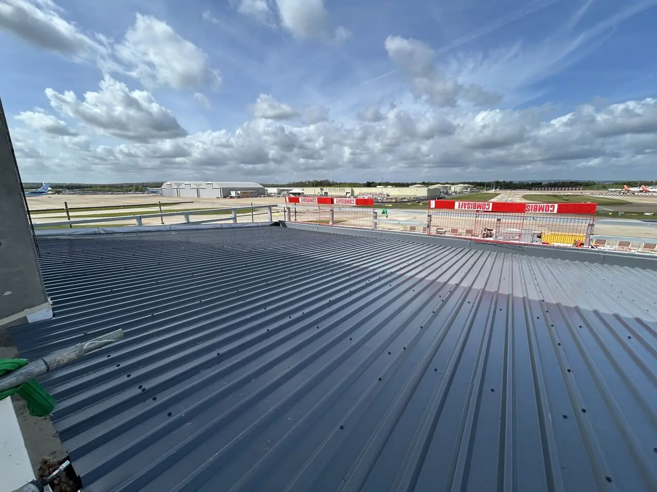 A newly installed dark grey profiled metal roof with the Gatwick airfield beyond