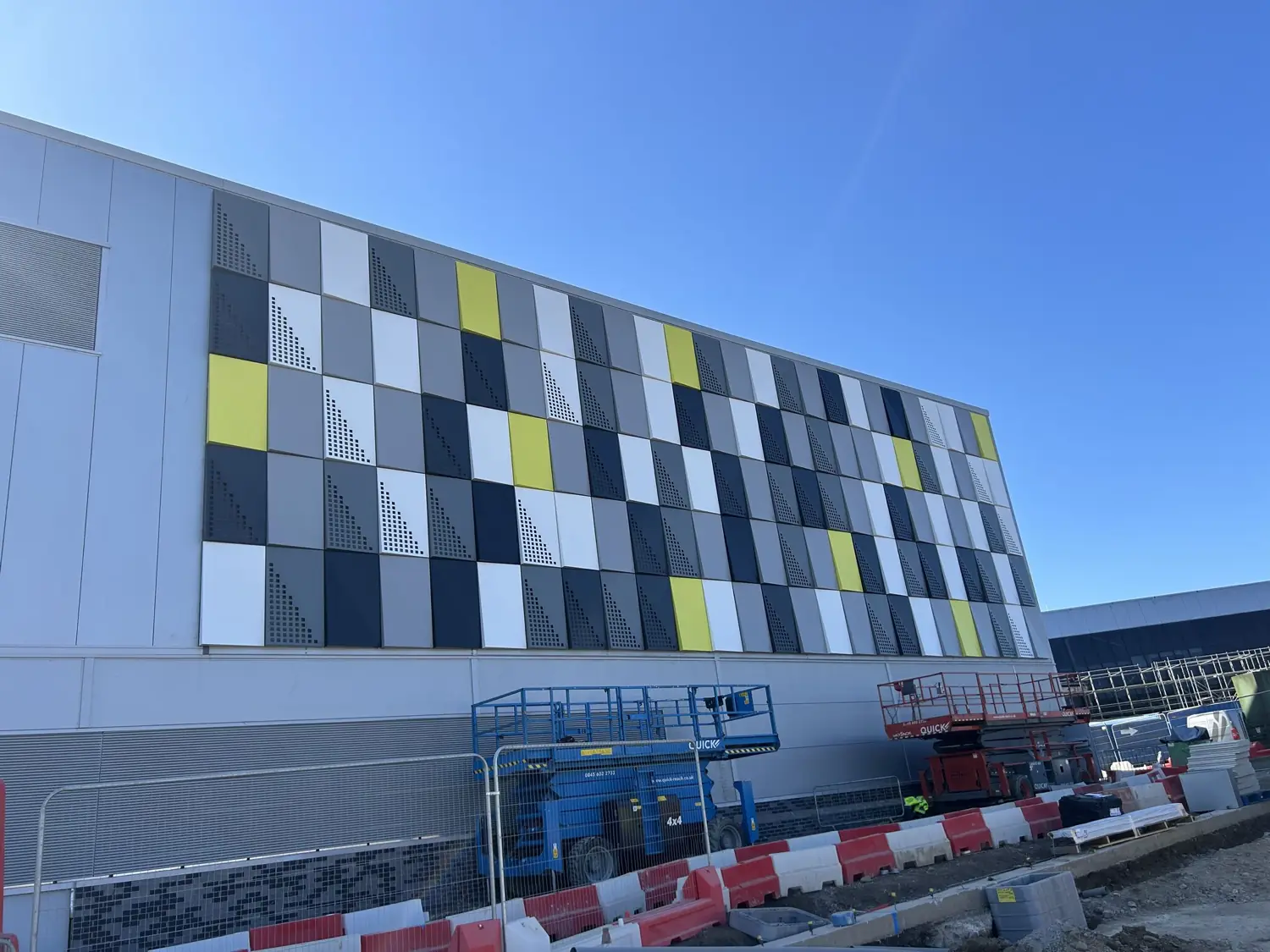 A facade of grey, white, navy and lime rainscreen cassettes, many perforated