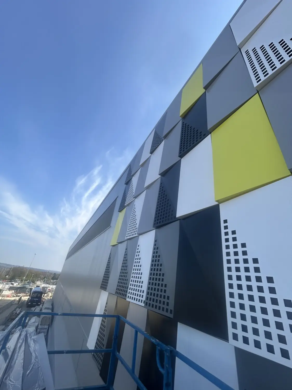 A raking view along a facade of grey, white, navy and lime rainscreen cassettes