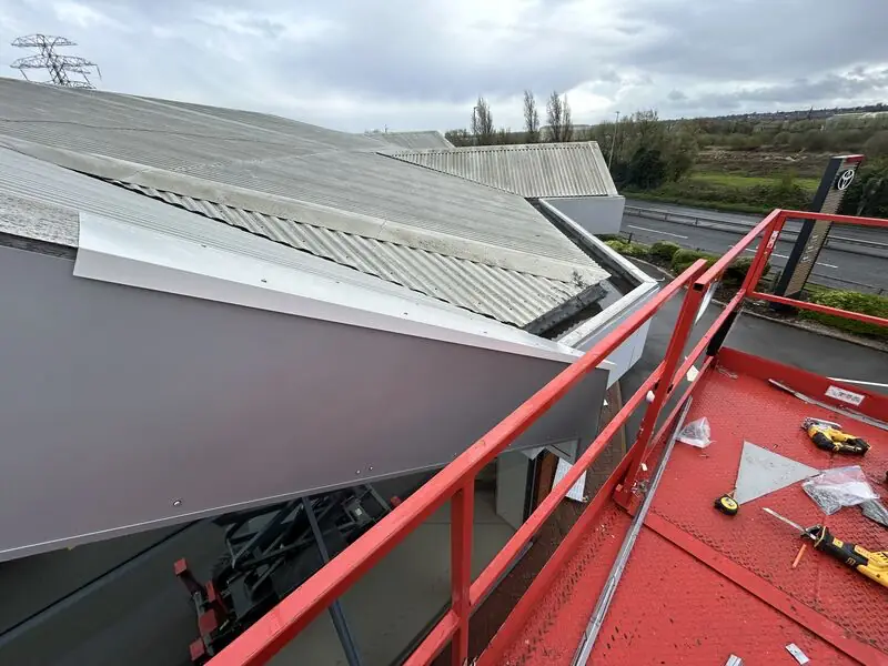 An ageing cement sheet dealership roof beside newly installed fascia and canopy metalwork