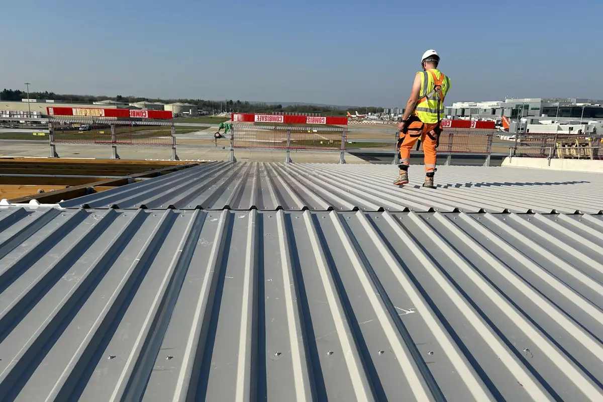 Roofer on the new standing seam roof at Gatwick Airport with the airfield behind