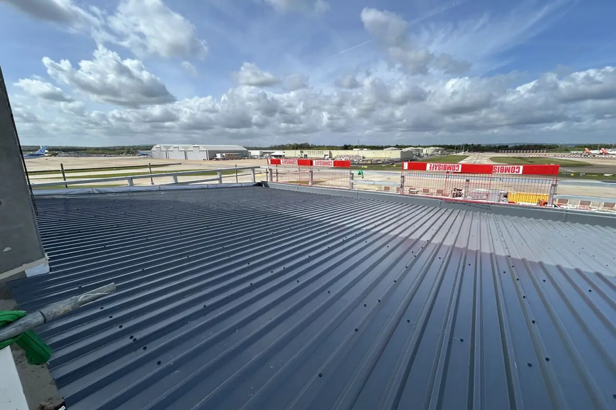 A dark grey profiled metal roof with aircraft hangars in the distance