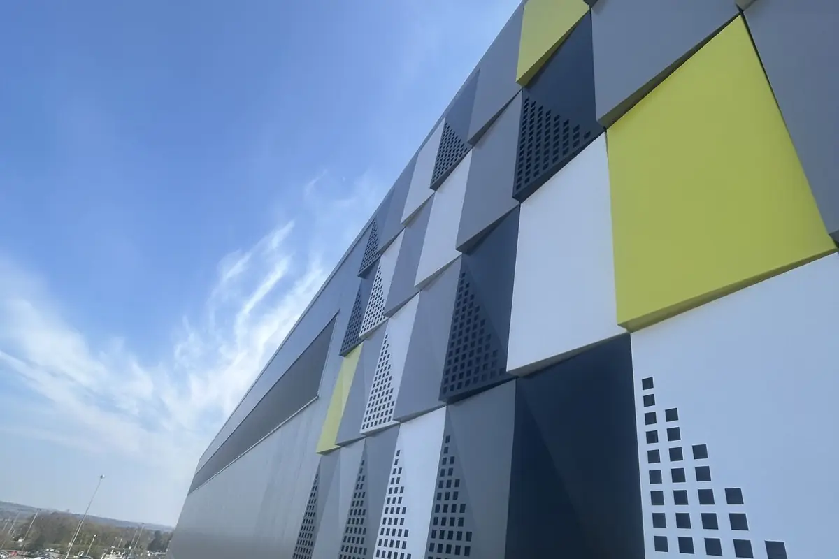 Raking view along a multi-coloured perforated rainscreen cassette facade