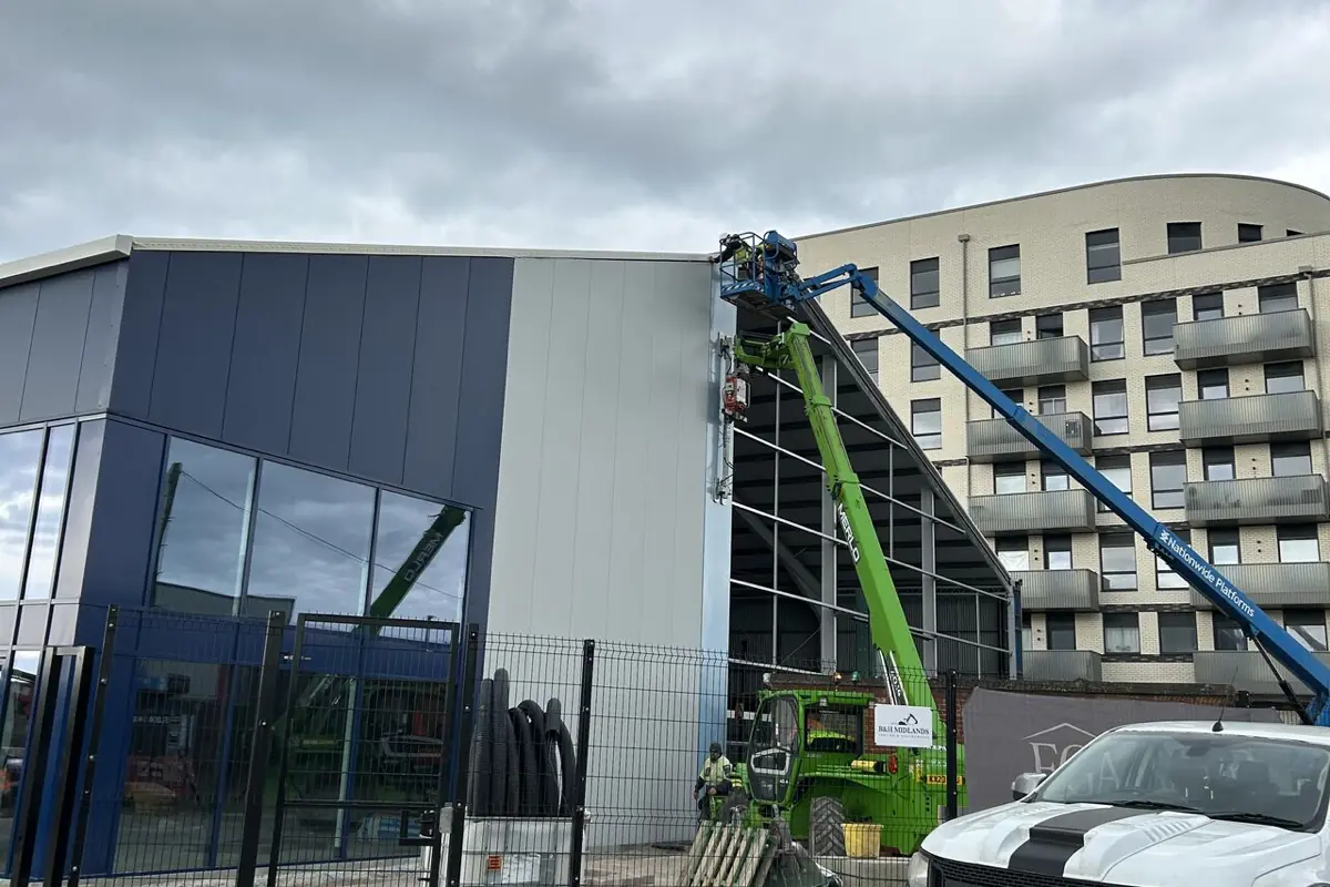 A unit being reclad in navy and silver panels with a telehandler and boom lift alongside