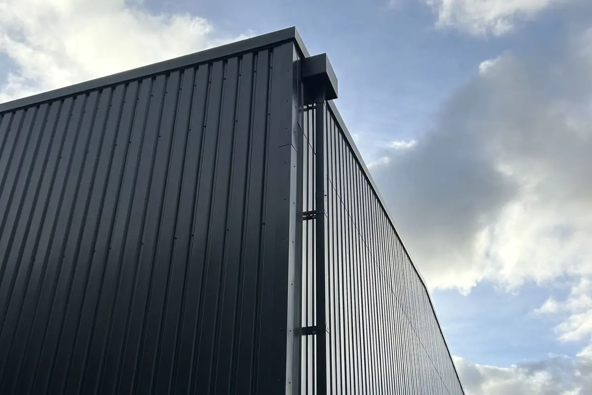 The corner of a unit in anthracite profiled cladding with a downpipe and hopper